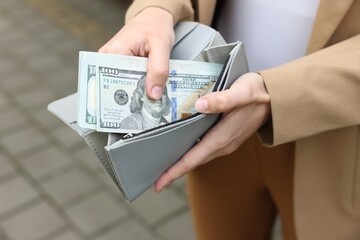 Woman putting money into wallet outdoors, closeup