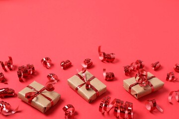 Shiny serpentine streamers and gift boxes on red background, above view. Space for text
