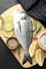 Fresh raw dourade with spices on black table, top view. Fish and seafood delicacies