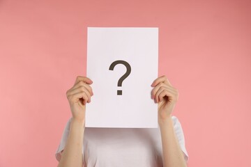 Anonymity. Woman hiding behind paper sheet with question mark on pink background