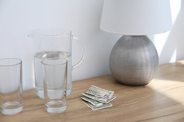 Tips, glasses and jug of water on wooden nightstand in hotel room, closeup