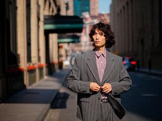 Portrait of handsome Chinese young man wearing gray suit posing in the street, young guy with black curly hair with urban background. Male fashion, cool Asian young man lifestyle.