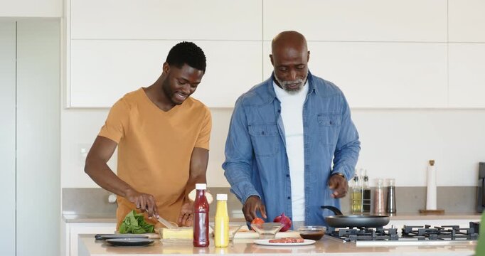African American father and son placing pan on stove making lettuce sandwiches at kitchen island