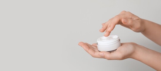 Female hands holding jar of cosmetic cream on grey background with space for text