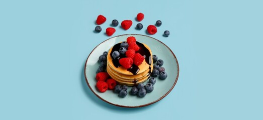 Plate of sweet pancakes with berries on light blue background