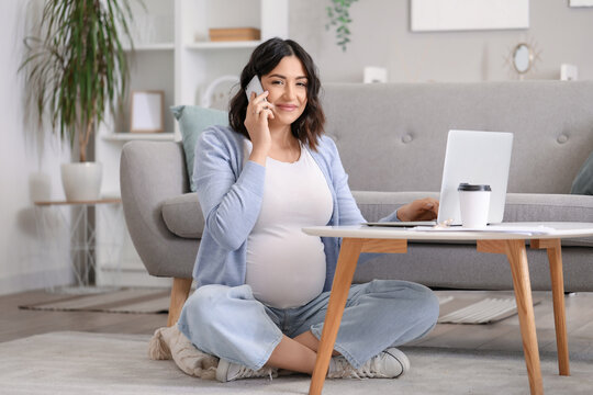 Working pregnant woman talking by mobile phone at home
