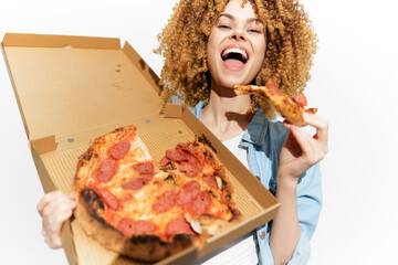 Happy woman enjoying pepperoni pizza in a takeaway box, showcasing joy with curly hair in a casual...