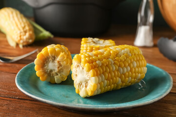 Plate with boiled corn cobs on wooden table