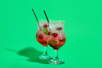 Glasses of fresh raspberry mojito on green background