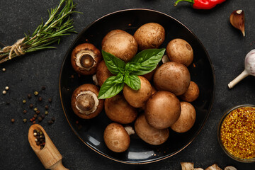 Plate with fresh mushrooms and different spices on black background