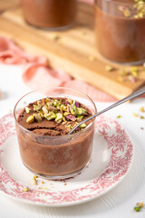 A close-up of a glass of chocolate pudding topped with chopped pistachios