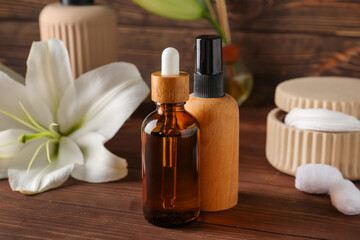 Bottles of cosmetic products, cotton pads and lily flowers on wooden background