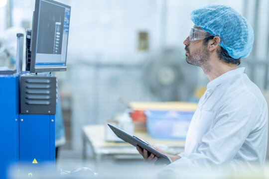 A supervisor in protective gear reviewing data on a computer screen at a food processing facility, holding a clipboard, emphasizing technology, quality control, and efficiency in industrial.