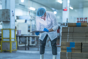 A food processing supervisor in protective gear inspecting packaging materials in a factory,...
