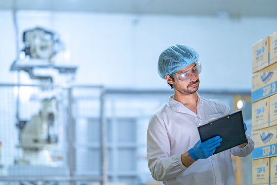 A factory worker in protective gear inspects stacked boxes in a food processing facility. The image highlights quality control, logistics, inventory management, and modern warehouse operations.