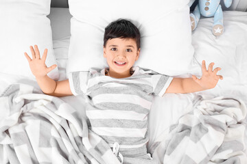 Cute happy little boy lying in bedroom