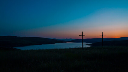 Obraz premium The silhouettes of three crosses are drawn on the horizon against the bright blue sky at sunset, framed by distant rolling hills and a calm lake in the background 