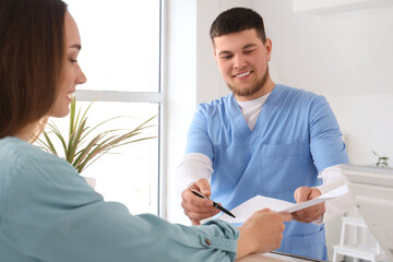Fototapeta premium Male receptionist giving filling form to patient in clinic