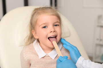 Pediatrician examining little girl with tongue depressor in clinic