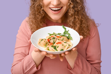Happy young woman with plate of tasty ravioli on lilac background
