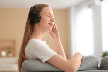 Naklejka premium Young pretty woman in headphones listening music in living room