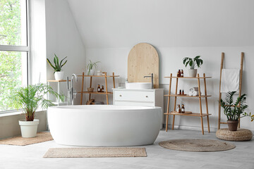 Interior of light bathroom with ceramic bathtub and houseplants