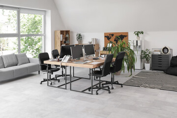 Interior of stylish office with workplaces, modern computers, grey sofa and armchairs