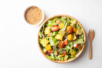 Top view of colorful vegetable salad in a rustic wooden bowl with Japanese sesame dressing on white background, Healthy, fresh, plant based eating concept