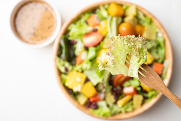 Top view of colorful vegetable salad in a rustic wooden bowl with Japanese sesame dressing on white background, Healthy, fresh, plant based eating concept