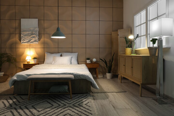Interior of bedroom with big bed, chest of drawers, bedside tables and glowing lamps at night