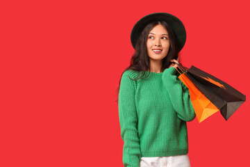 Beautiful young Asian woman with shopping bags on red background