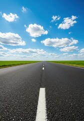 A long, straight asphalt road extends into the distance under a blue sky with white clouds