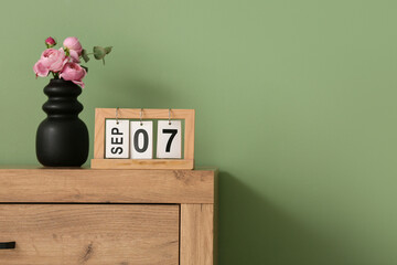 Calendar with date 7 September and flowers on wooden table near color wall