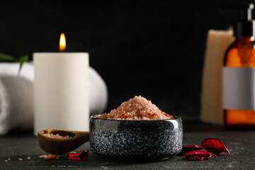Beautiful spa composition with bowl of sea salt and petals on black background, closeup