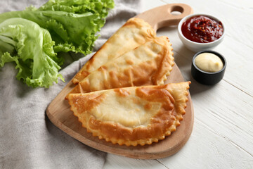Board with tasty chebureks, fresh lettuce and sauces on white wooden table