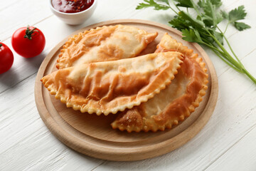 Tasty chebureks, tomatoes and parsley on white wooden background
