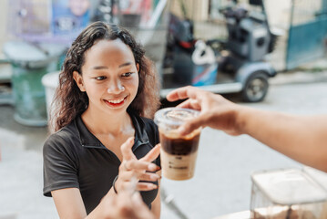 Barista gives a freshly made iced caramel latte to a young female customer at a coffee stand, ready to enjoy on the go.