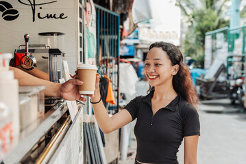 Barista gives a freshly made iced caramel latte to a young female customer at a coffee stand at a southeast asian city.