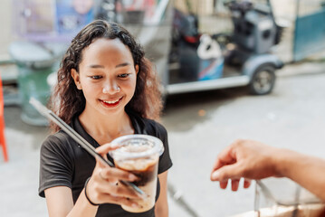Barista gives a freshly made iced caramel latte to a young female customer at a coffee stand at a southeast asian city.