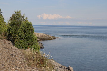 A bay with trees and a beautiful blue horizon in Charlevoix in Quebec. Coastline and geology and nature formation in Charlevoix in Canada. Summer calendar with a vast river and Canada landscape.