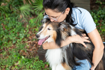 Woman holding senior dog hugging and kissing on the head showing love