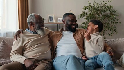 Three generations of a happy black family laughing and bonding together on comfortable sofa in their living room