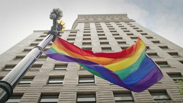 A rainbow pride flag waves in the wind next to a vintage street lamp in  San Francisco, California, USA. The flag represents LGBTQ+ pride and equality.
