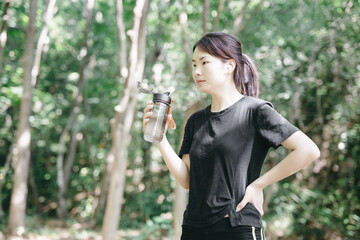 Young woman drinking water in a forest during outdoor activity