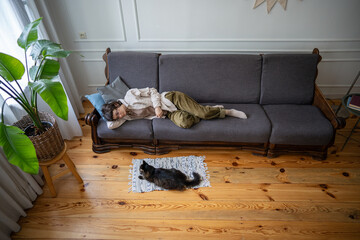 Depressed woman in decline lying half asleep on sofa, motionless with only feline companion for...