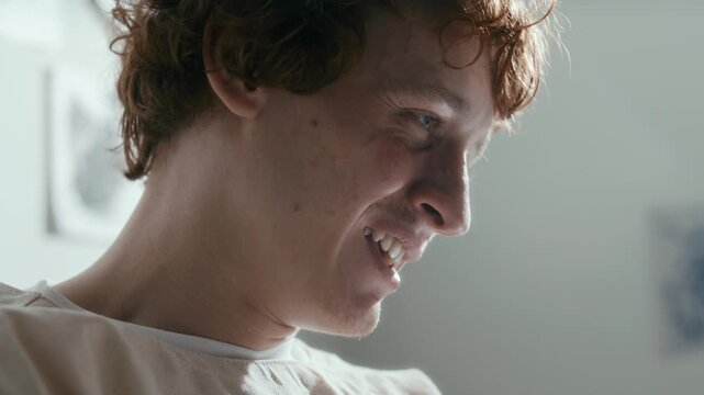 Young male patient in straitjacket speaking with tension during mental therapy session in sunlit psychiatric ward. Close-up view