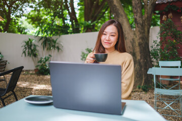 Portrait image of a young woman drinking coffee while working on laptop computer in the outdoors cafe