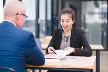 Young businesswoman explaining financial report to senior businessman in modern office, smiling and engaged in discussion