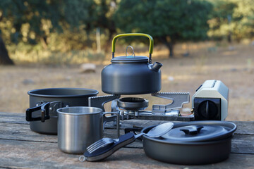 Camping kettle warming on a portable stove with various cookware items arranged on a weathered...