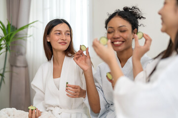 Diverse group of beauty women enjoy skincare routine, applying cucumber eye masks for hydration and...